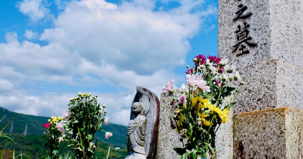 青空の下に建つ石碑と手を合わせるお地蔵様