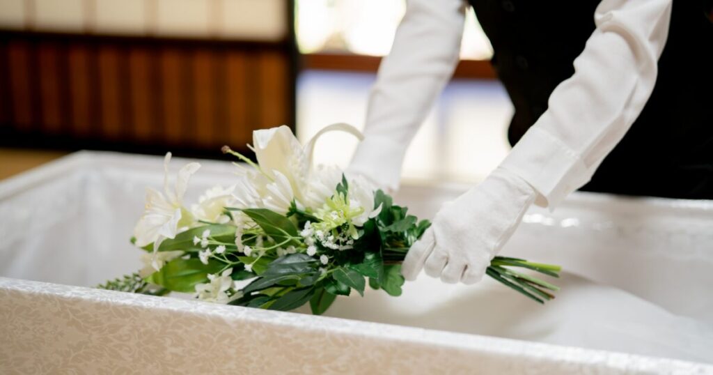 白い手袋をした係員が白いユリの花束を棺の中に丁寧に納める様子