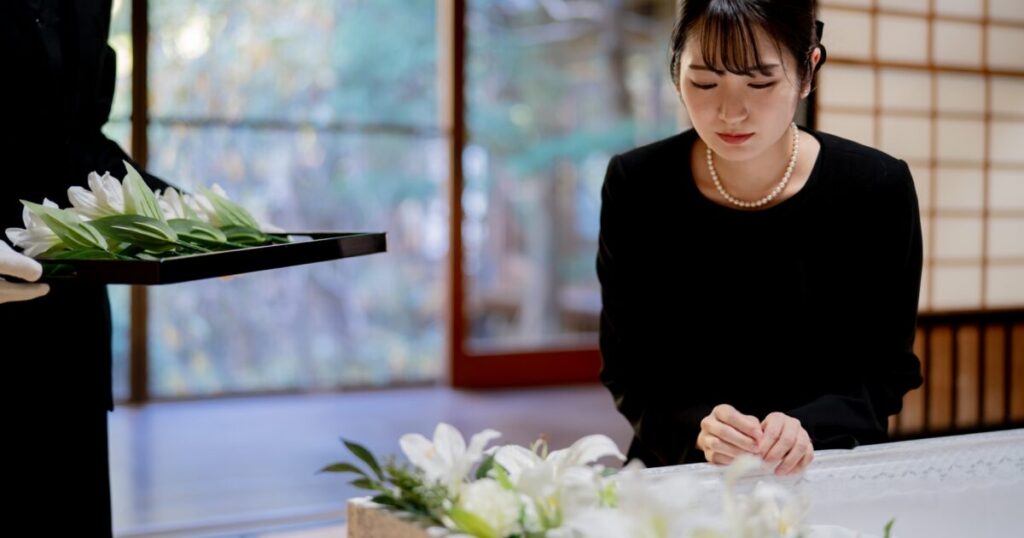 喪服の女性が棺の前で手を合わせている姿