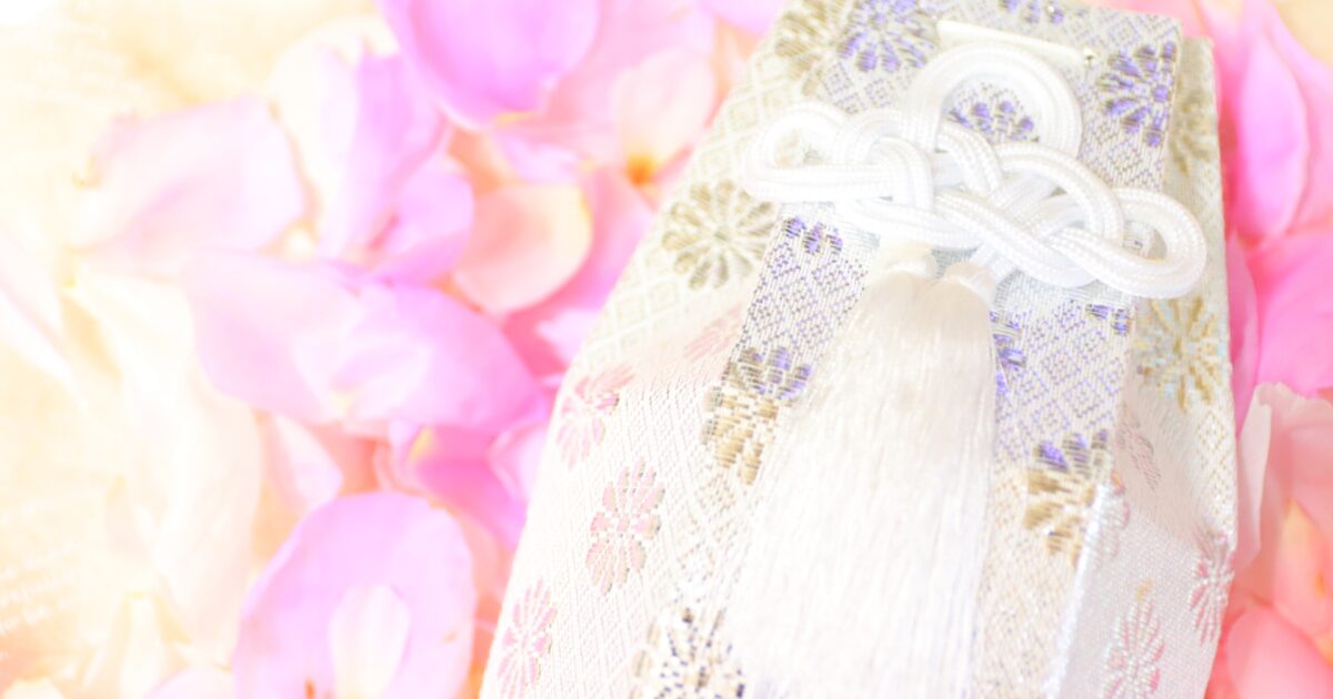 淡い光に包まれた白と銀の骨壷袋と花びら