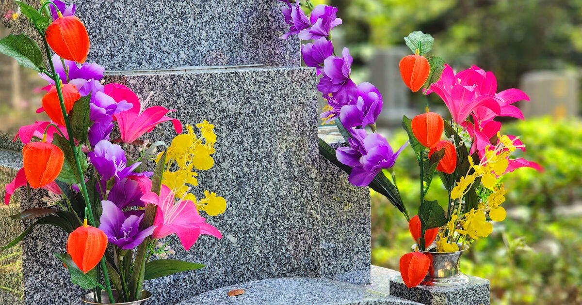 白御影石の墓に供えられたカラフルな花と墓地の風景