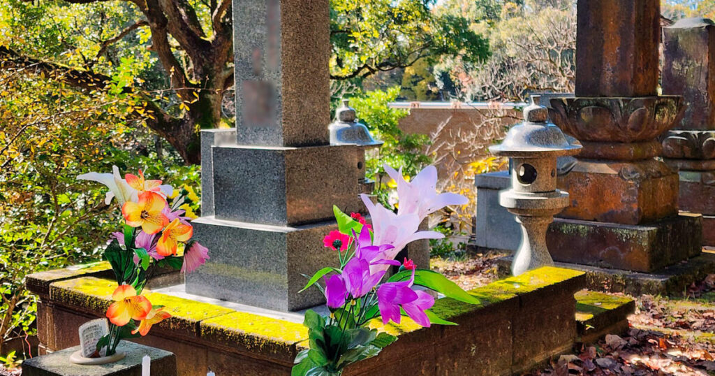 木漏れ日の中に佇む苔むした墓石と供えられた色鮮やかな花