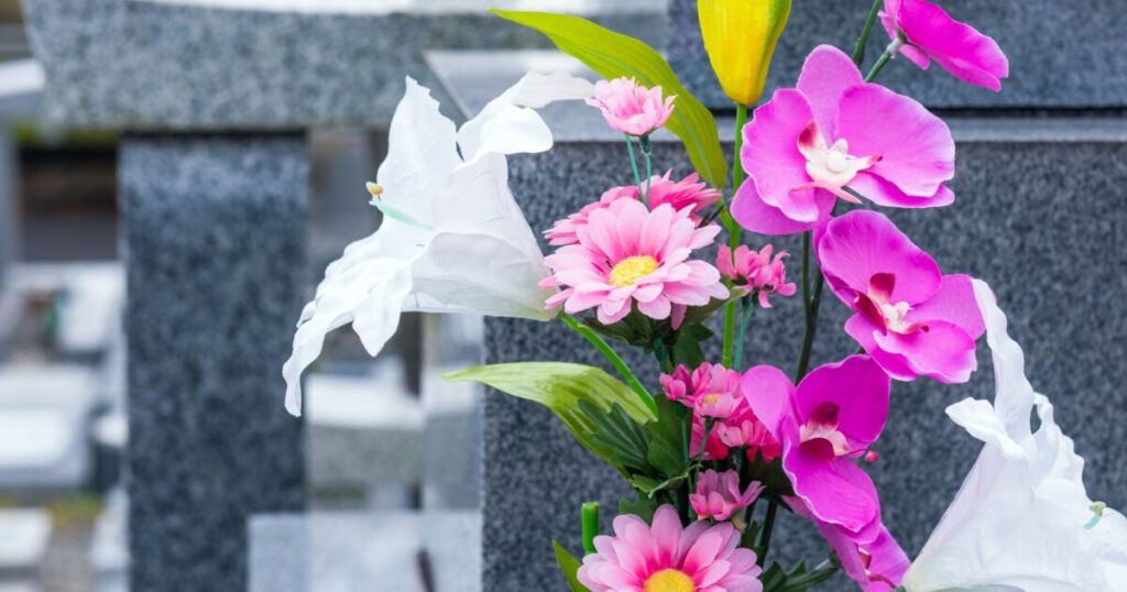 灰色の墓石の前に飾られたピンクと白の造花