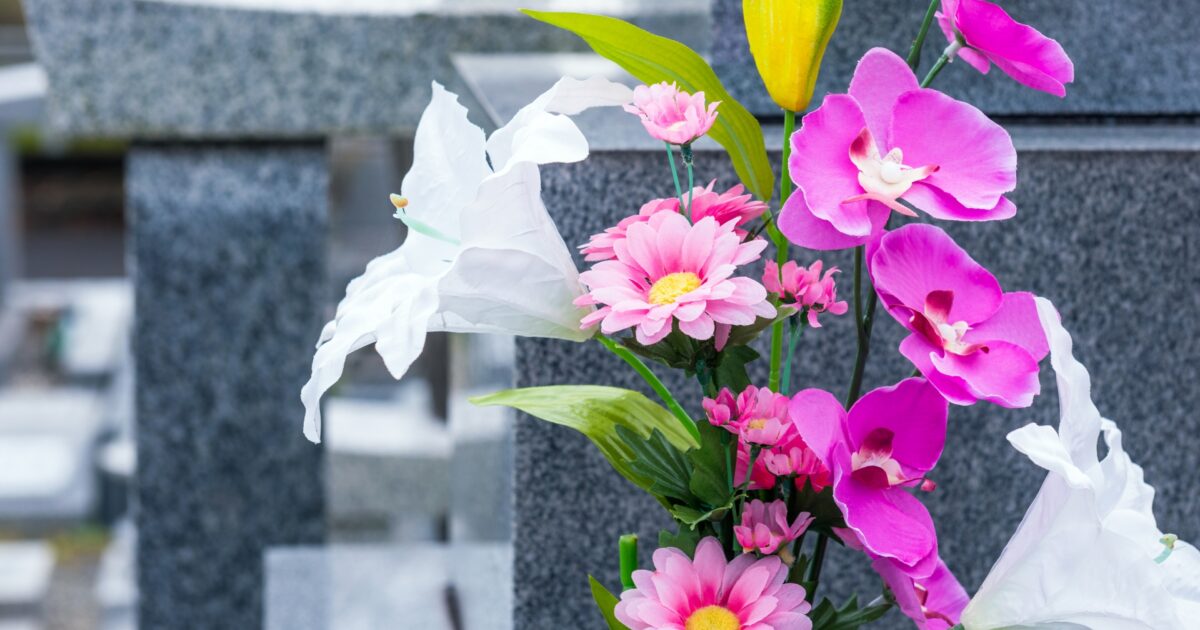 灰色の墓石の前に飾られたピンクと白の造花