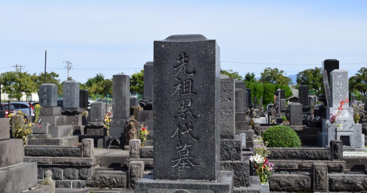 青空の下に並ぶ墓石と「先祖累代墓」と刻まれた黒御影石の墓