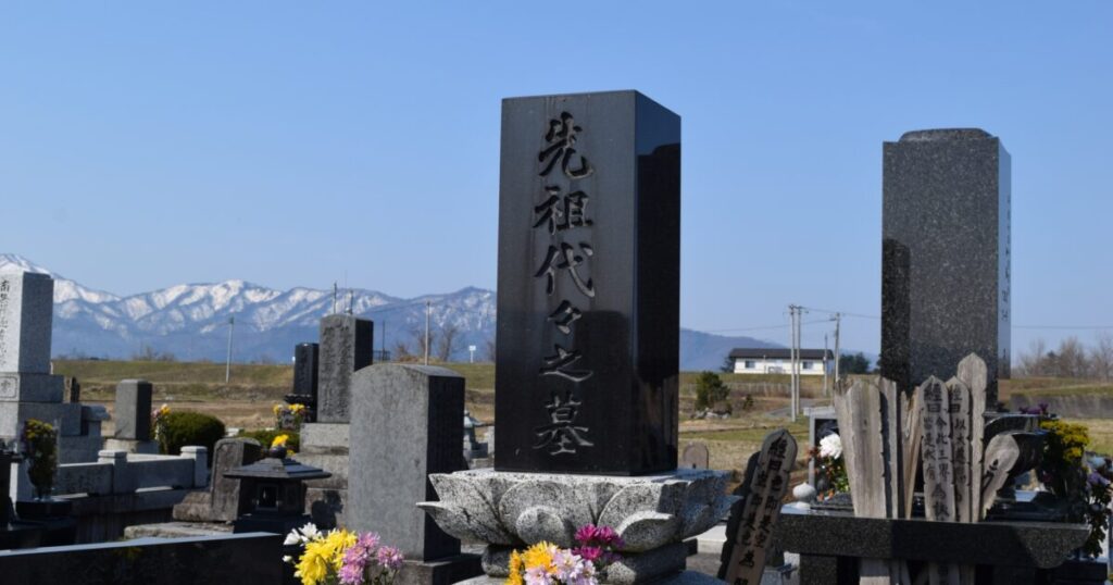 雪山を背景に立つ「先祖代々之墓」と刻まれた黒御影石の墓