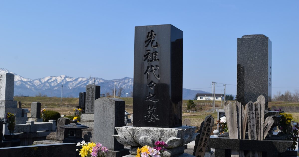 雪山を背景に立つ「先祖代々之墓」と刻まれた黒御影石の墓